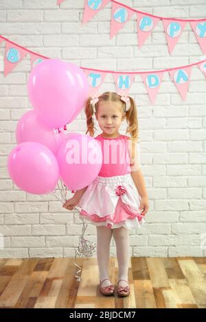 Little cute girl holding party balloons on brick wall background Stock Photo