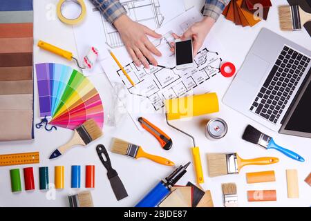 Decorator using a phone. Color swatches and painting tools all around on table Stock Photo