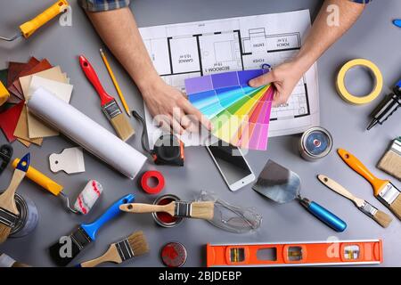 Decorator's hands holding color swatches. Project drawing and paint tools on work table Stock Photo