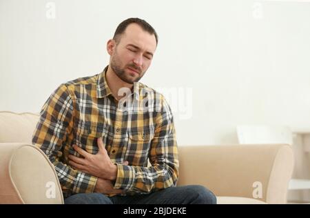 Handsome young man suffering from stomach ache at home Stock Photo