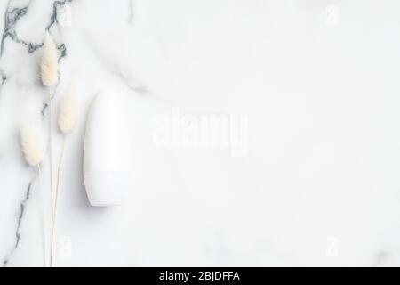 Roll-on deodorant packaging with dry flowers on marble background. Blank antiperspirant bottle, sweat protection concept. Flat lay, top view Stock Photo
