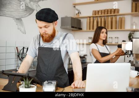 Coffee Business Concept - Young handsome bearded bartender, barista or manager posting the order from guest in digital tablet menu at modern coffee Stock Photo