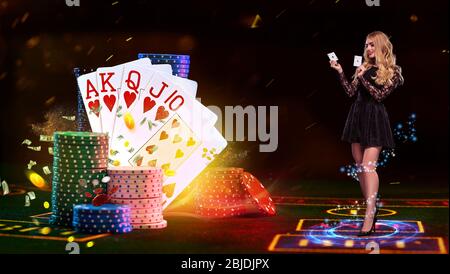 Girl in black dress is holding two aces, smiling, posing on green playing table with blue neon circle on it, next to stacks of colorful chips and play Stock Photo
