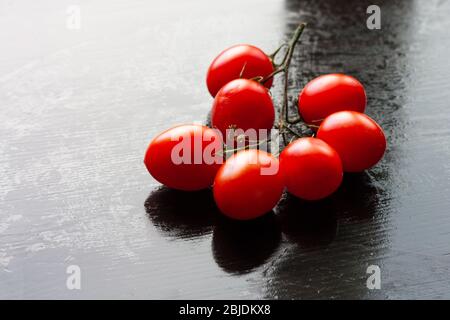 Piccadilly tomato bunch. Fresh juicy sweet tomatoes for traditional Mediterranean cuisine. Black wet background Stock Photo