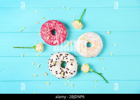 Delicious colourful donuts and flowers on blue wooden background Stock Photo