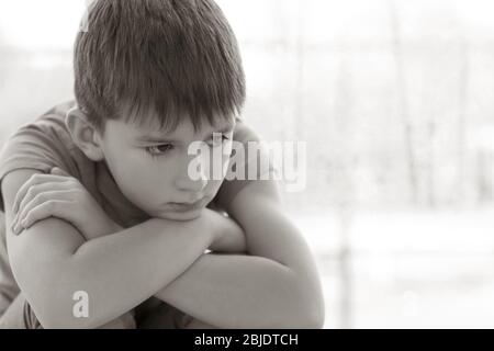 Sad little boy sitting on windowsill Stock Photo