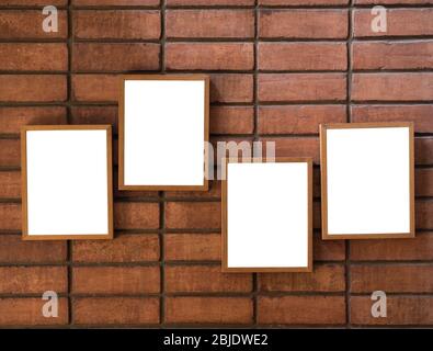 Four white blank vertical picture frames hanging on the red brick wall background. Stock Photo