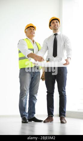 Handsome engineer and worker discussing plan of works while standing inside new building Stock Photo