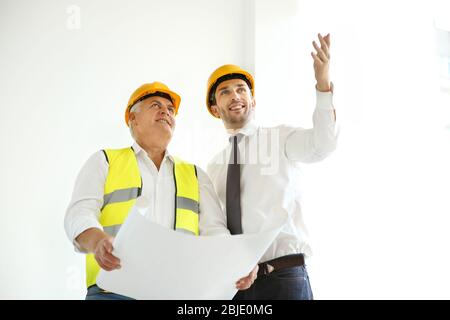 Handsome engineer and worker discussing plan of works while standing inside new building Stock Photo