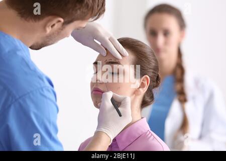Plastic surgeon applying marks onto young woman's face prior to operation Stock Photo