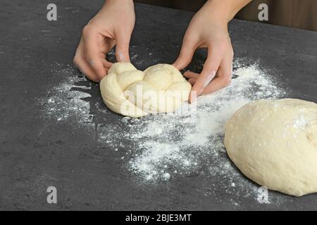 Woman preparing tasty braided bun on kitchen table, close up Stock Photo