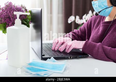 Woman agent call center operator in face mask, gloves works online from home on laptop. Remote work. Social distancing to prevent COVID-19 coronavirus Stock Photo
