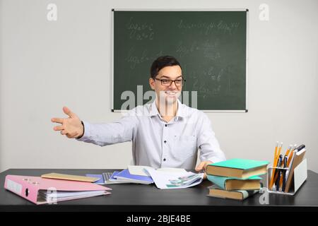 Handsome young teacher sitting at table in classroom Stock Photo