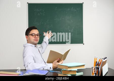 Handsome young teacher sitting at table in classroom Stock Photo