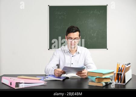 Handsome young teacher sitting at table in classroom Stock Photo