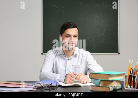 Handsome young teacher sitting at table in classroom Stock Photo