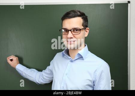 Handsome young teacher writing on blackboard in classroom Stock Photo