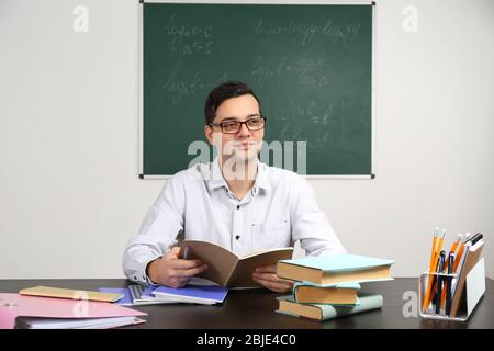 Handsome young teacher sitting at table in classroom Stock Photo