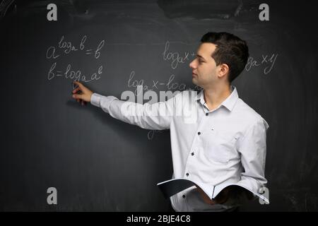Handsome young teacher explaining math formulas written on blackboard Stock Photo