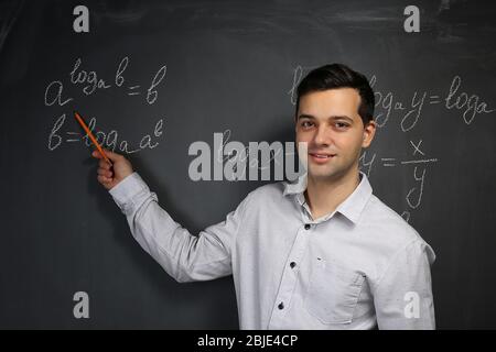 Handsome young teacher explaining math formulas written on blackboard Stock Photo