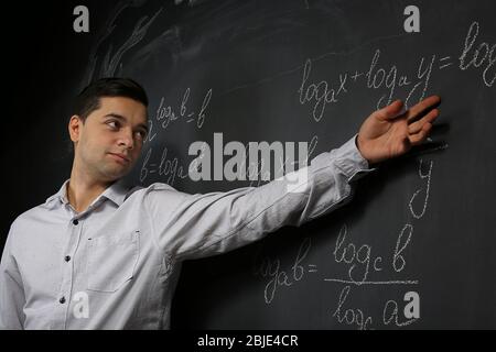 Handsome young teacher explaining math formulas written on blackboard Stock Photo