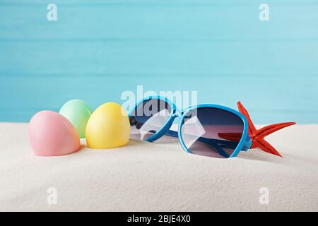 Easter eggs with sand and sunglasses, on wooden blue background Stock Photo