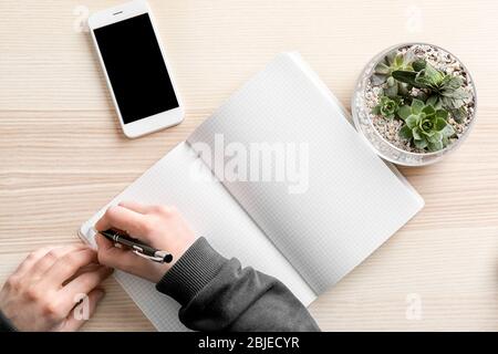 Male hand writing something on notebook. Workspace with florarium in glass vase with succulents Stock Photo