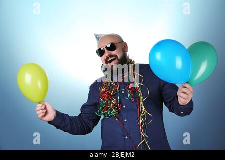 Funny fat man with birthday hat and balloons on color background Stock Photo