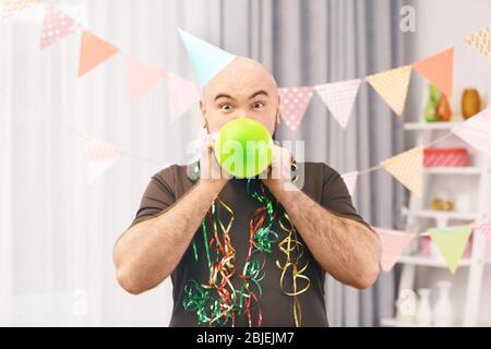 Funny fat man inflating balloon at birthday party Stock Photo