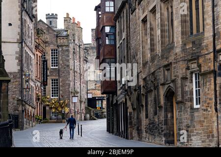 Edinburgh, Scotland, UK. 29 April 2020. Views of Edinburgh Old Town as coronavirus lockdown continues in Scotland. Streets remain deserted and shops and restaurants closed and many boarded up. Scottish Government now recommends public to wear face masks. Man walking dog on empty Royal Mile. Stock Photo