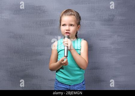 Cute little girl with microphone on color background Stock Photo