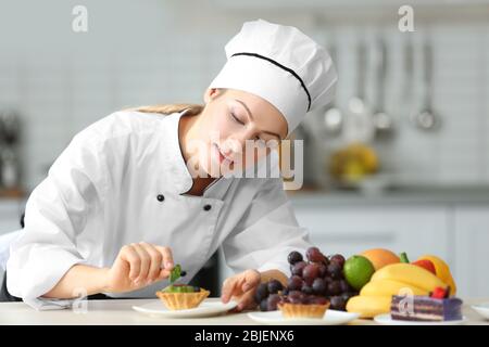 Female chef decorating fruit tartlet in kitchen Stock Photo