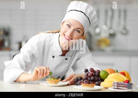 Female chef decorating fruit tartlet in kitchen Stock Photo