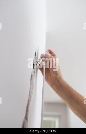 Low angle view of male hand checking presence of electrical current in wire coming from a wall. Stock Photo