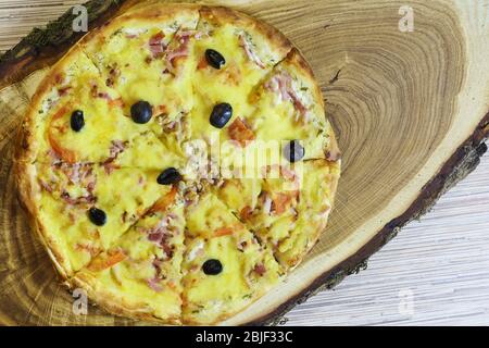 Yellow hearty fresh pizza with cheese and olives on a natural wooden Board. Italian food Stock Photo