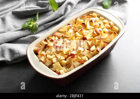 Tasty bread pudding with apples in baking dish on table Stock Photo