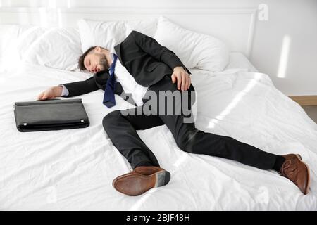 Dressed in business suit man fell asleep on bed in light room Stock Photo