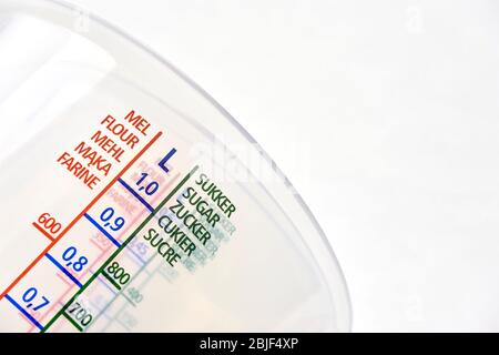 Detail of transparent plastic measuring cups with words flour and sugar in danish, english, german, polish and french on white background. Stock Photo