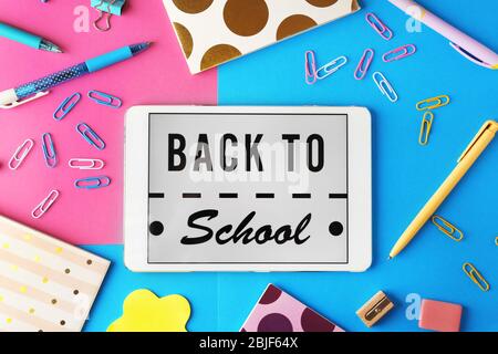 Tablet with BACK TO SCHOOL message and stationery on color background Stock Photo
