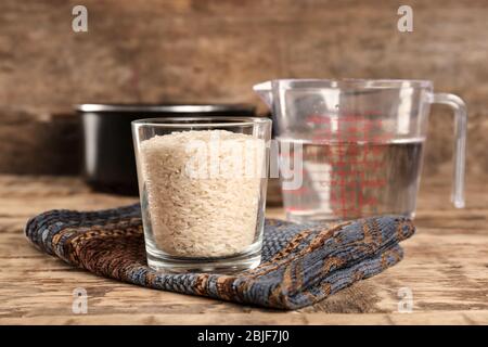 Glass of rice and measuring jug with water on wooden table Stock Photo