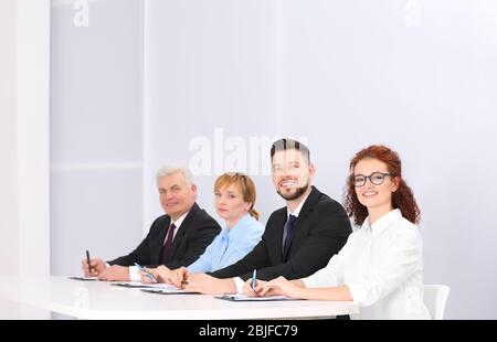 Group of four business people in elegant suits sitting at working desk in light auditorium Stock Photo