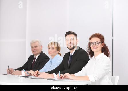 Group of four business people in elegant suits sitting at working desk in light auditorium Stock Photo