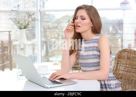 Smoking young woman working on laptop in light room Stock Photo