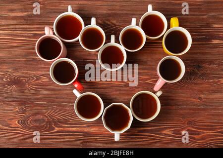 Delicious tea in cups forming heart on wooden background Stock Photo