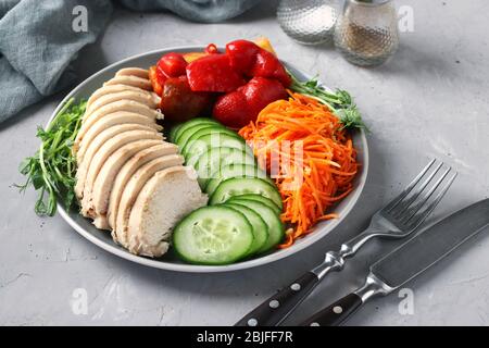 Buddha Bowl with baked chicken, fresh cucumber, peas microgrines, carrots and sweet pepper on a gray concrete background. Concept for clean and Stock Photo