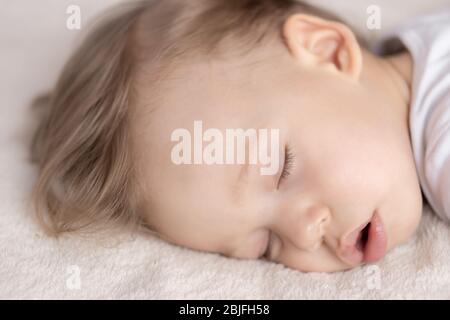Childhood, sleep, rest, family, lifestyle concept - close-up portrait of a cute little boy of 2 years old in a white body sleeping on a beige bed at Stock Photo