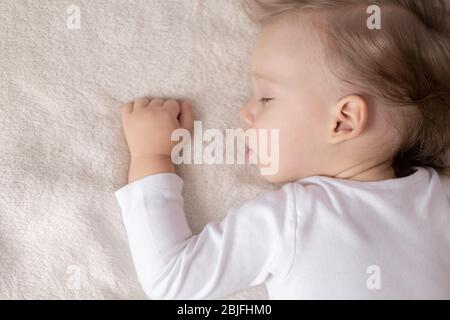 Childhood, sleep, rest, family, lifestyle concept - close-up portrait of a cute little boy of 2 years old in a white body sleeping on a beige bed at Stock Photo