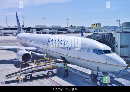 LOS ANGELES, CA -26 APR 2020- An airplane from United Airlines (UA) and a baggage handler wearing a face mask during the COVID-19 crisis at the Los An Stock Photo