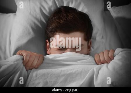 Young scared man lying in bed at home Stock Photo