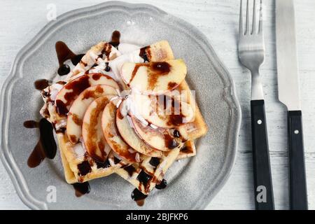 Delicious waffles with apple slices, syrup and sugar powder on plate Stock Photo